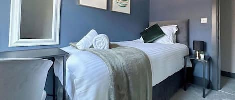 Une chambre d’hôtel comprenant un lit, un bureau, une chaise, une table de chevet et des œuvres d’art murales.