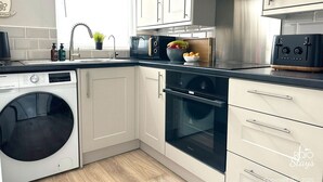 A modern kitchen with white cabinets, a built-in oven, a washing machine, and a sink with a faucet.