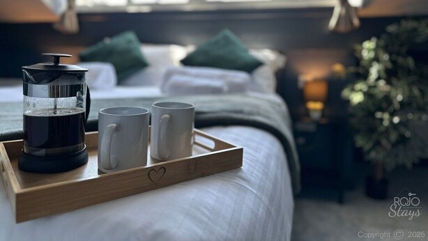 A cozy hotel room with a bed, a coffee maker, and two mugs on a tray.