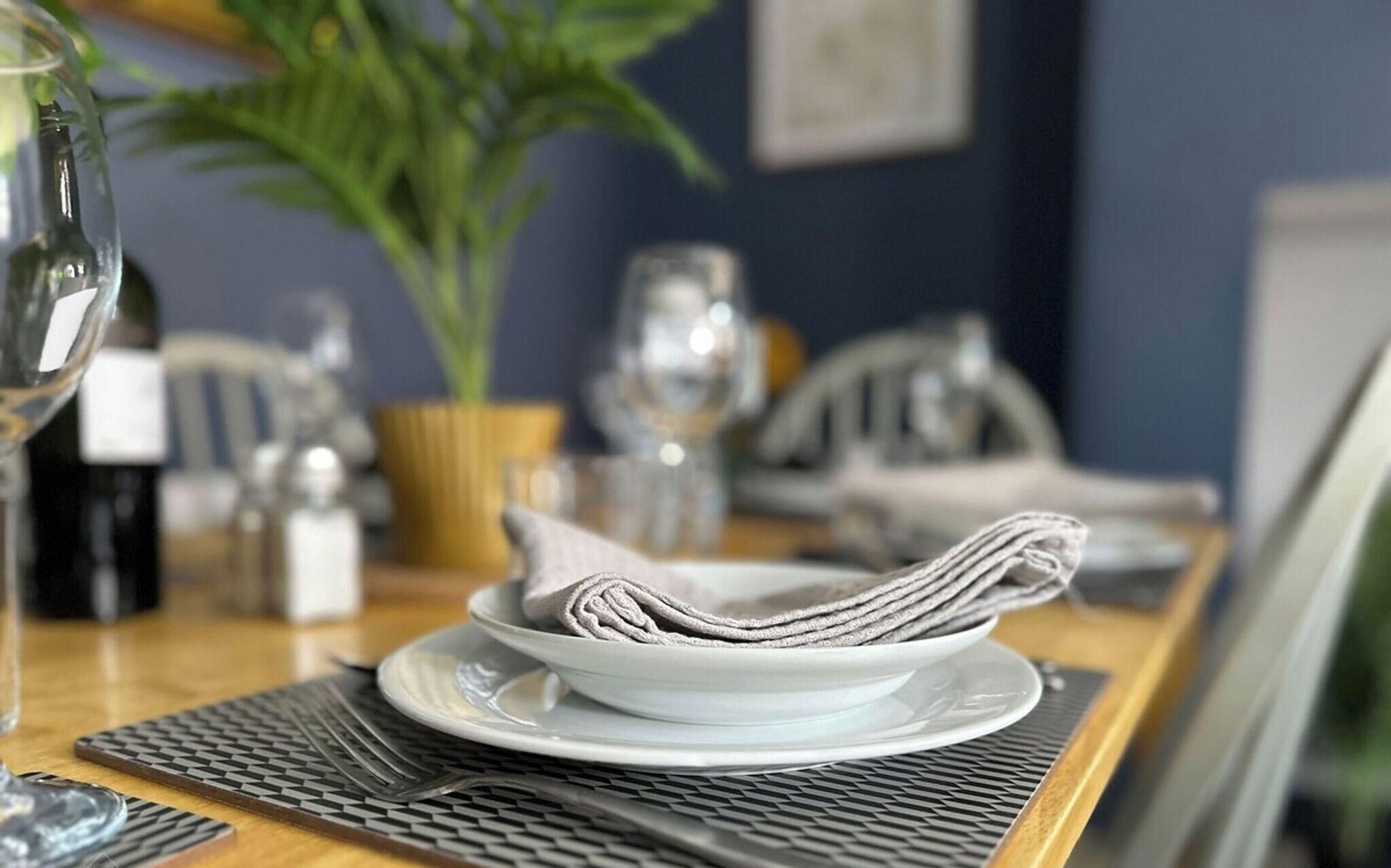 Una mesa de comedor con un mantel doblado, una botella de vino y una planta en maceta.