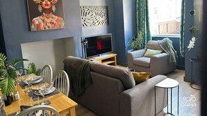 A modern living room with a sofa, a dining table set, a TV, and decorative elements like a painting and a wall art piece.