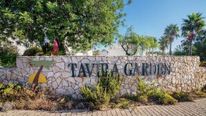 En stenmur med texten ”TAVIRA GARDEN” och ett litet träd framför.