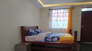A bedroom with a bed, a nightstand, a window with curtains, and a door. - Antonio Accommodation Kericho (Kericho)