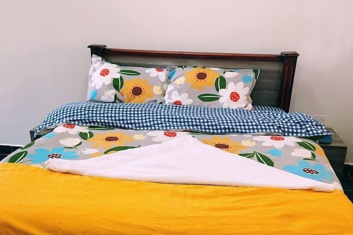 Ein Bett mit einem blumigen Überwurf, karierten Kissen und einer gelben Decke.