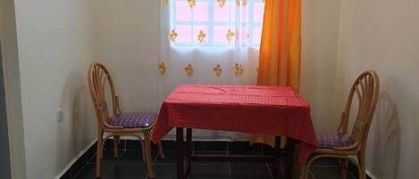 Una habitación con una mesa, dos sillas, un ventanal con cortina y piso de baldosas.