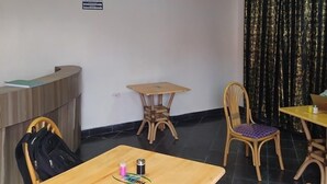 A room with a reception desk, a wooden table with chairs, a small round table, and a curtain. - Antonio Accommodation Kericho (Kericho)