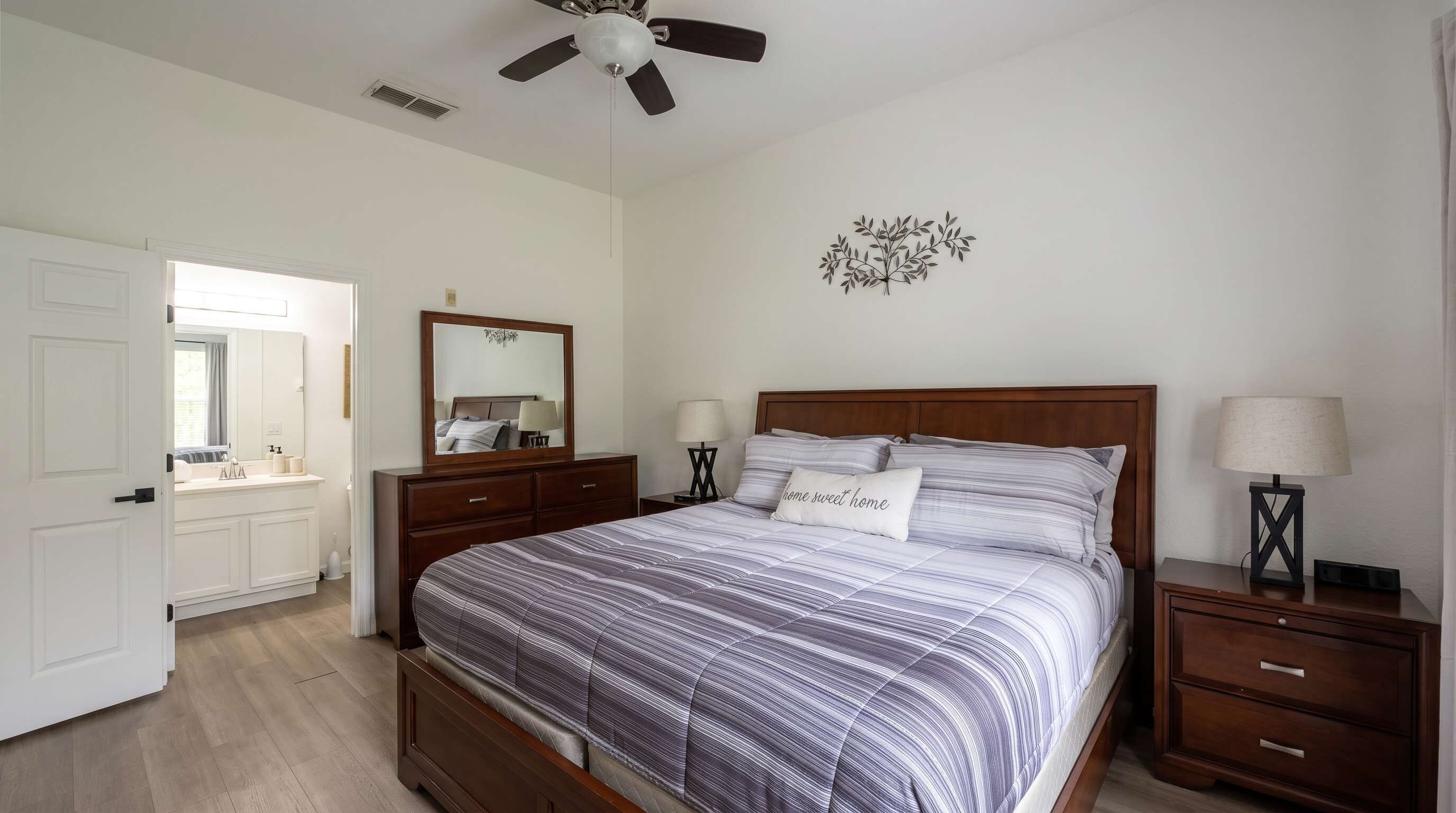 Une chambre à coucher comprenant un lit, des tables de chevet, un ventilateur de plafond, un miroir et un élément de décoration murale.