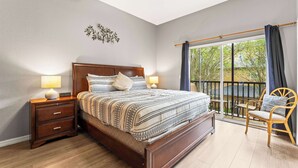 Un dormitorio con una cama grande, mesitas de noche de madera, un ventilador de techo y vistas al exterior a través de un ventanal corredero.
