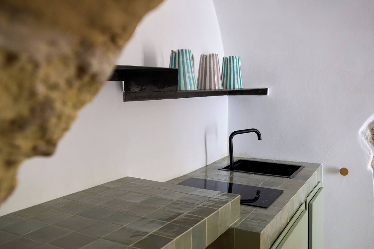 A modern kitchen with a sleek black faucet, a tiled countertop, and a shelf with striped vases.