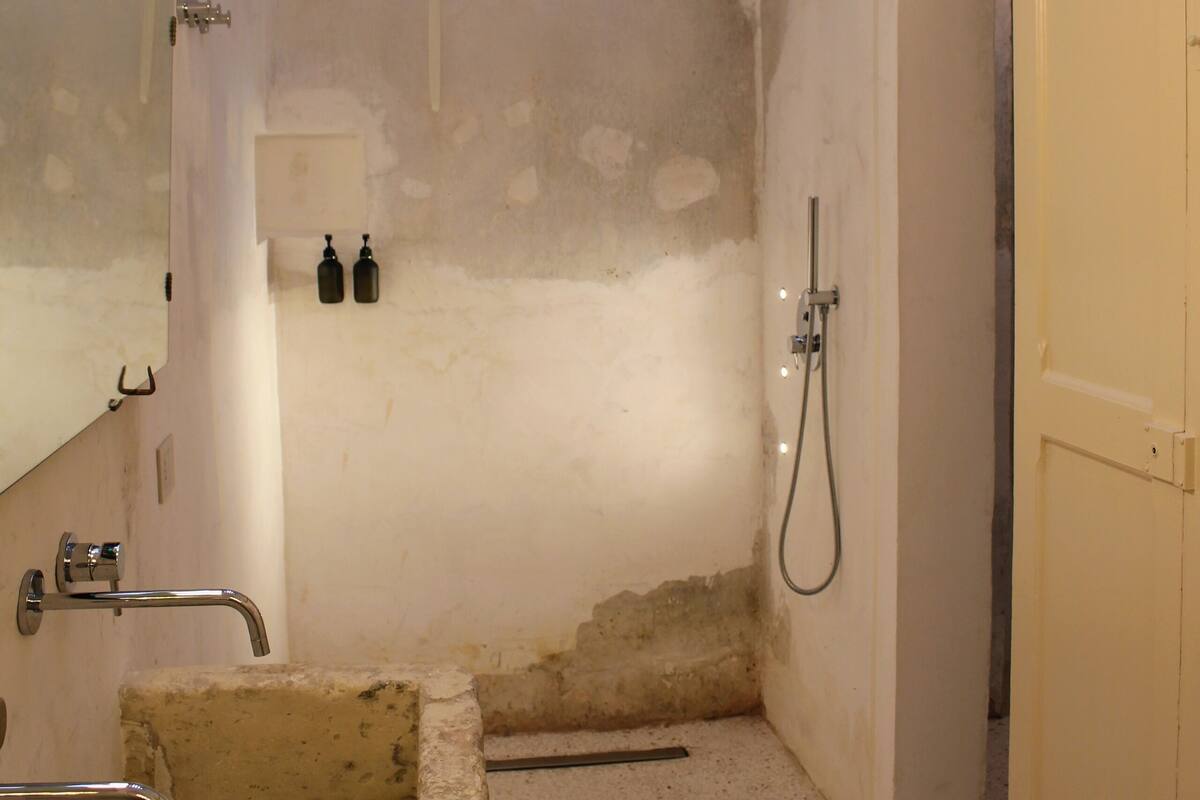 A small, narrow bathroom with a bathtub, a shower, and a toilet. There is a mirror on the left wall and a towel rack above the shower.
