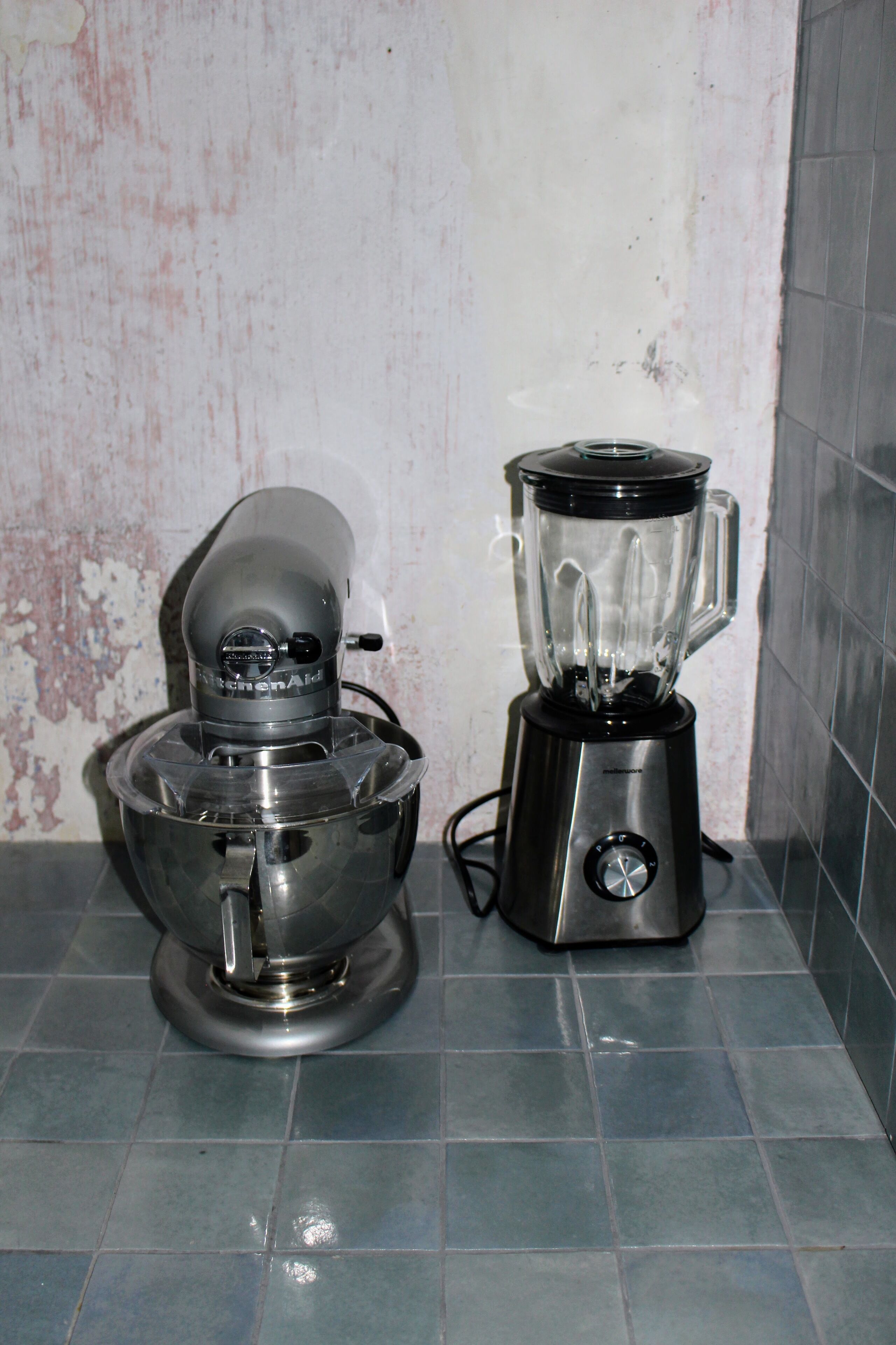 A kitchen with a blender and a food processor on a tiled floor.
