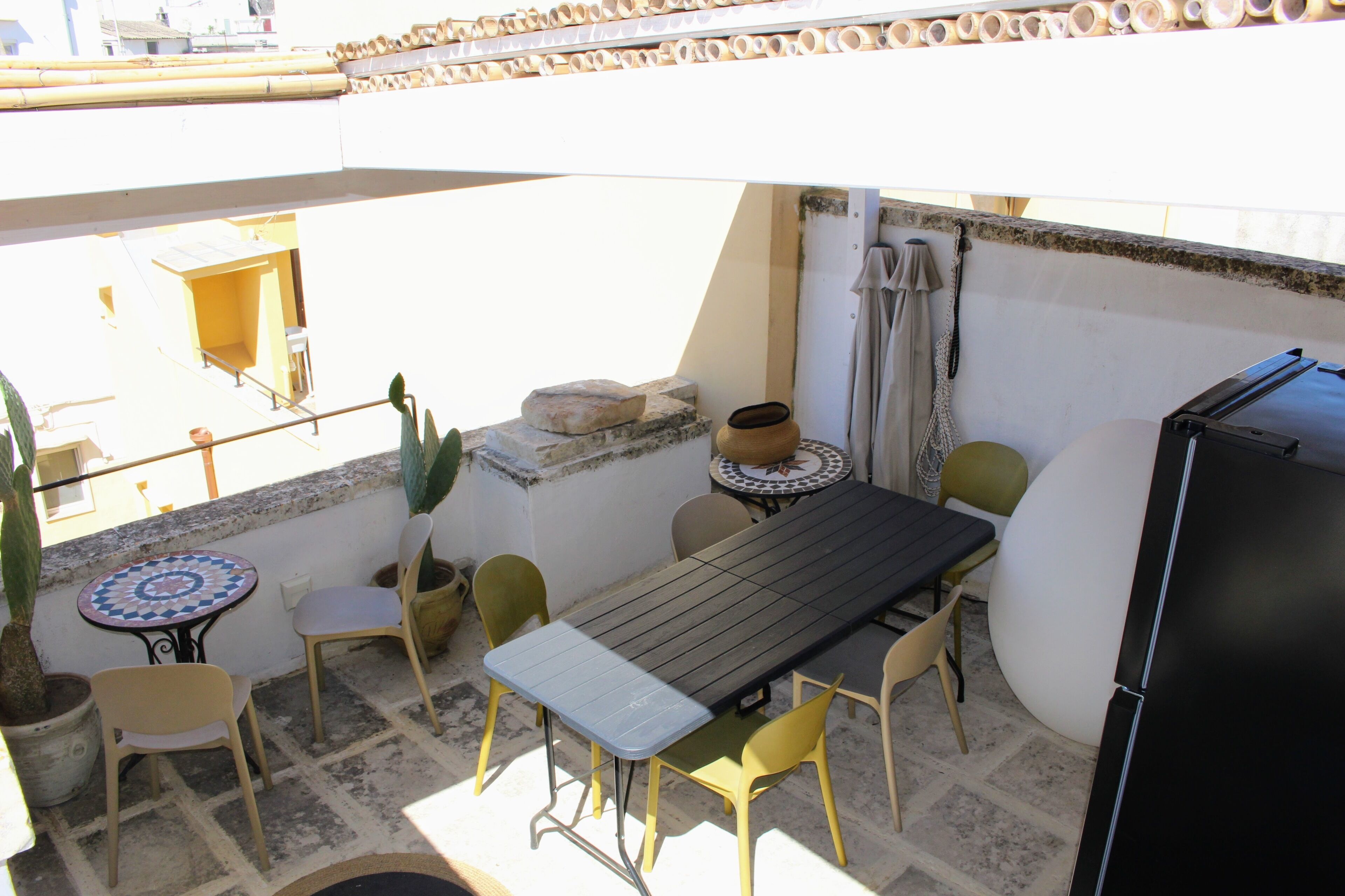 A small outdoor patio with a table and chairs, a refrigerator, and potted plants.