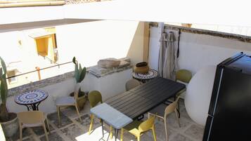 A small outdoor patio with a table and chairs, a refrigerator, and potted plants.
