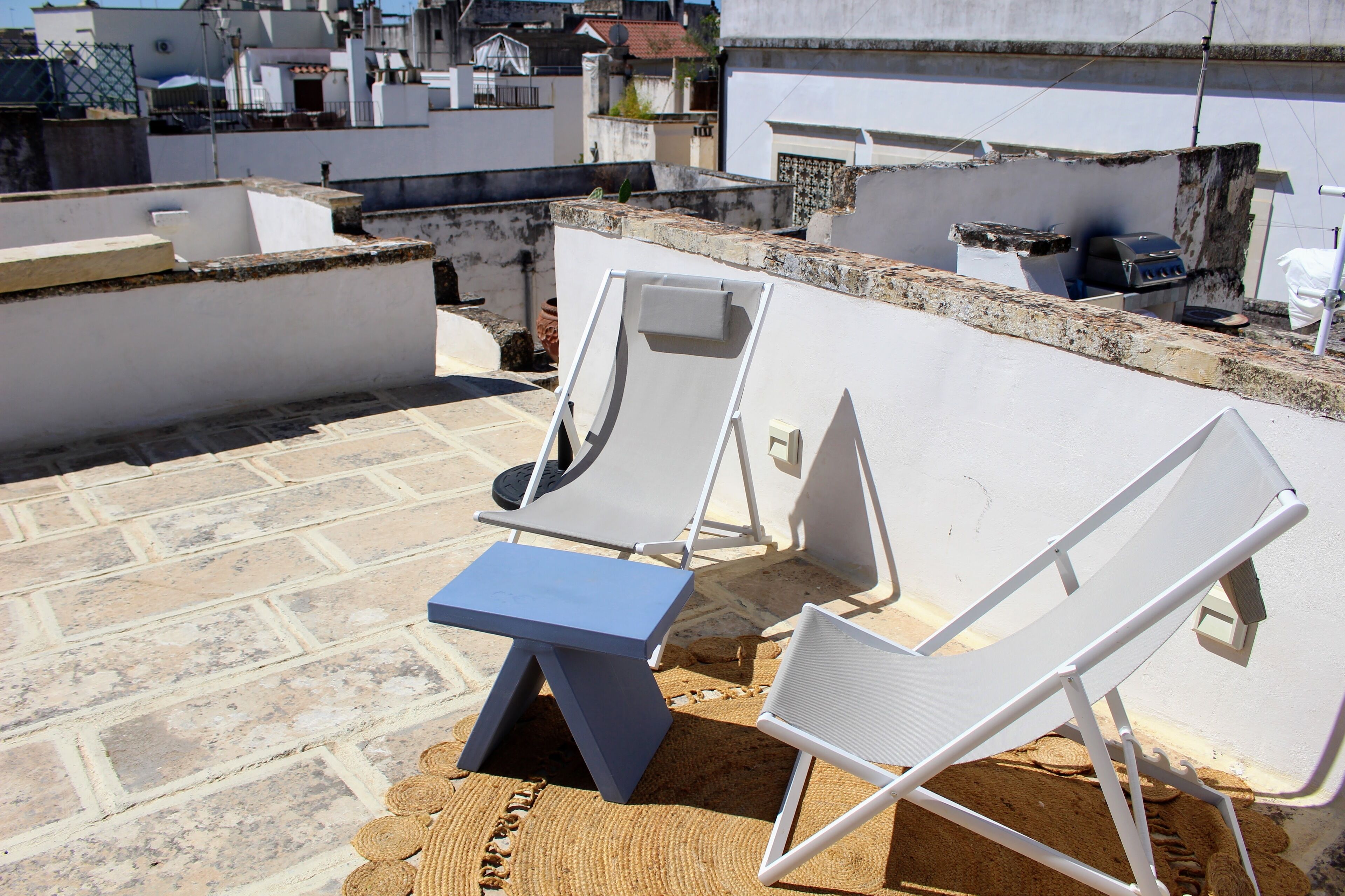 Une terrasse sur le toit, avec deux chaises longues blanches et une petite table, entourée d’un sol en pierre et de murs blancs.