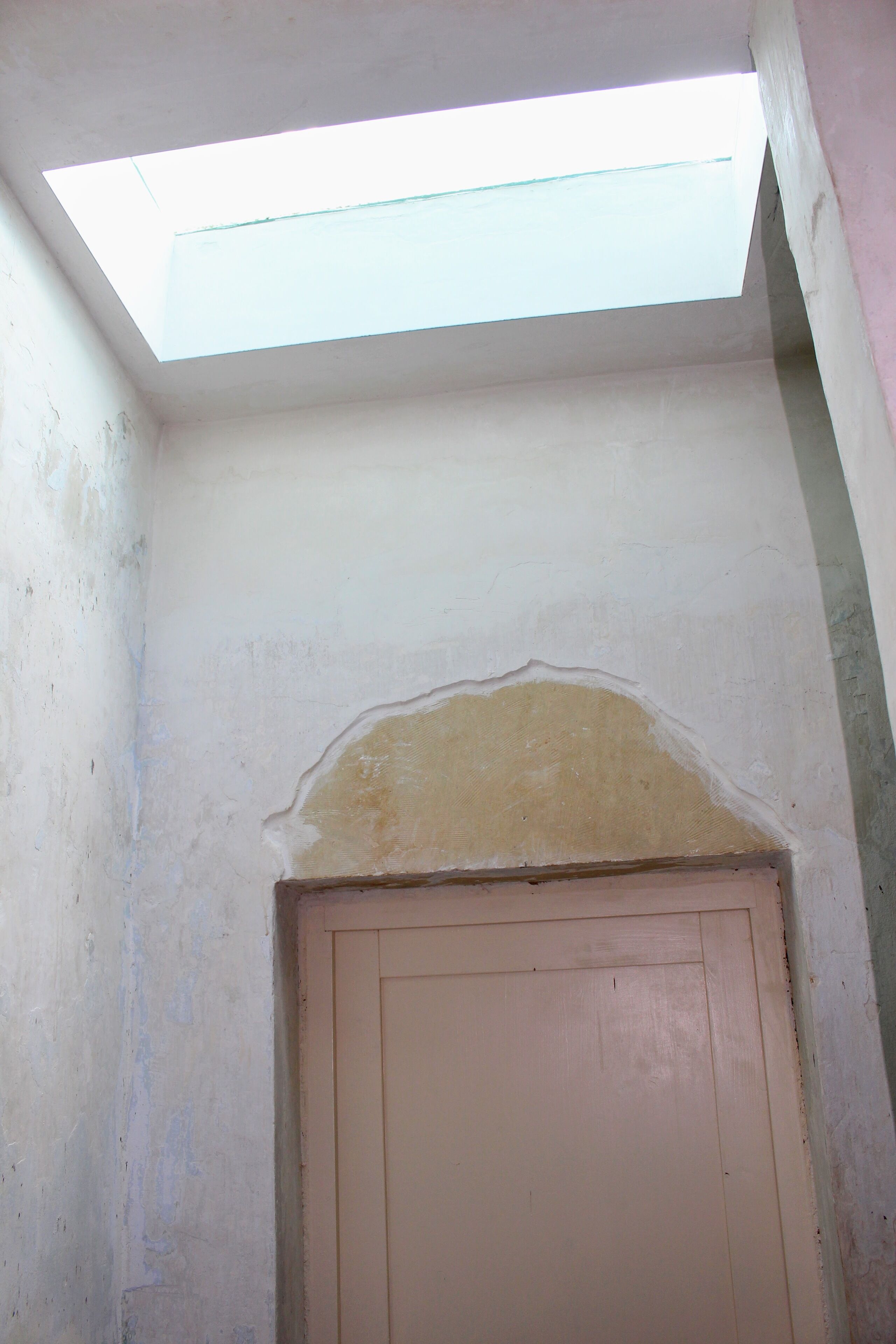 A room with a skylight, a door, and a wall with peeling paint.