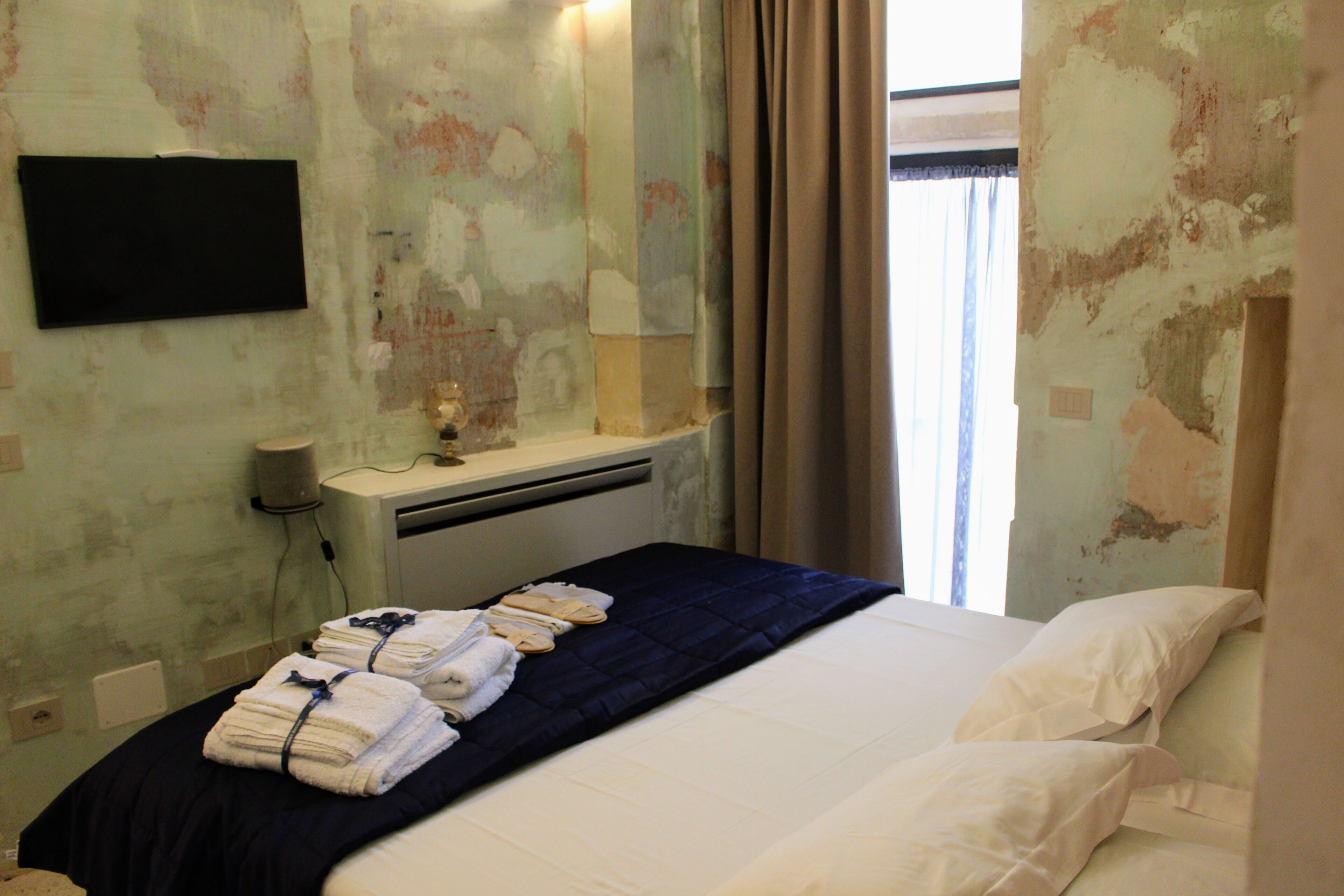 A hotel room with a bed, a bedside table with a lamp, a mirror, and towels on the bed.