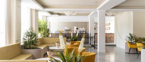 A modern lobby with seating areas, potted plants, and a visible bar area in the background.