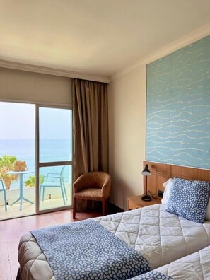A hotel room with a bed, a chair, a nightstand, and a view of the ocean through a large window. - Hotel Santa Rosa (Torrox)
