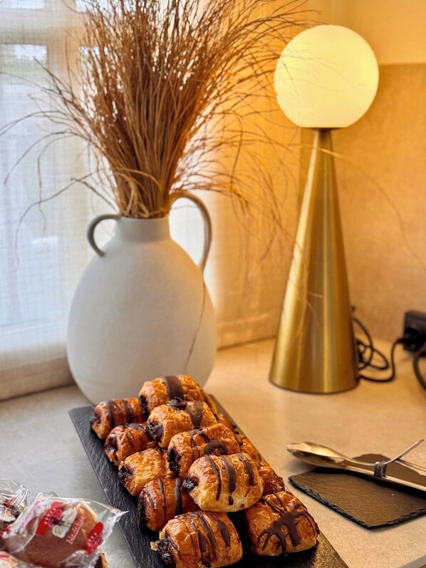 A table with pastries, a vase with dried plants, and a lamp.