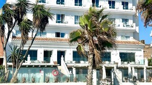 A multi-story hotel with balconies, palm trees, and a clear blue sky.