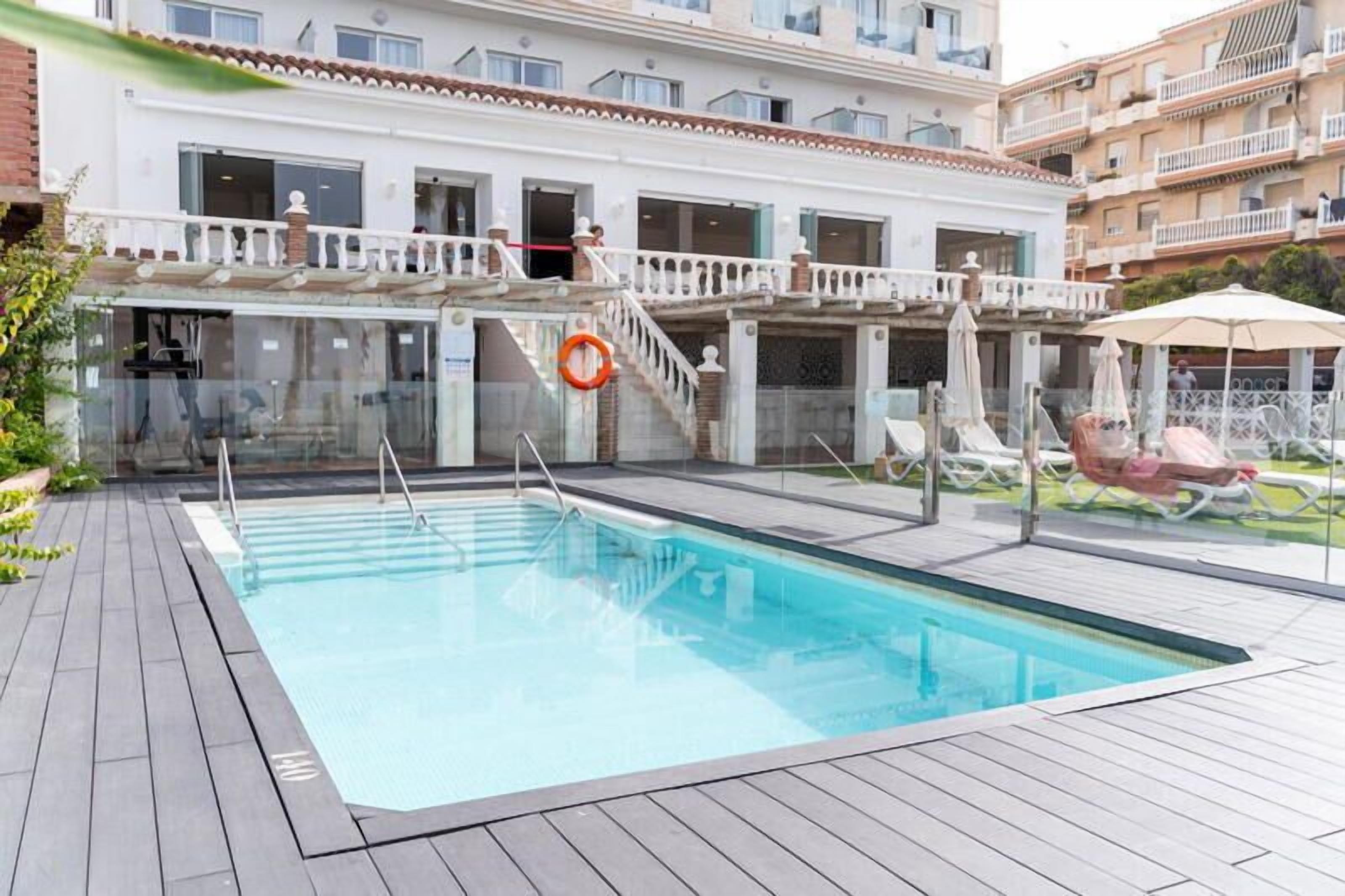 A swimming pool with a wooden deck, a lifebuoy, and a lounge area with umbrellas.