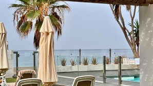 An outdoor seating area with chairs and tables, a palm tree, and a view of the ocean.