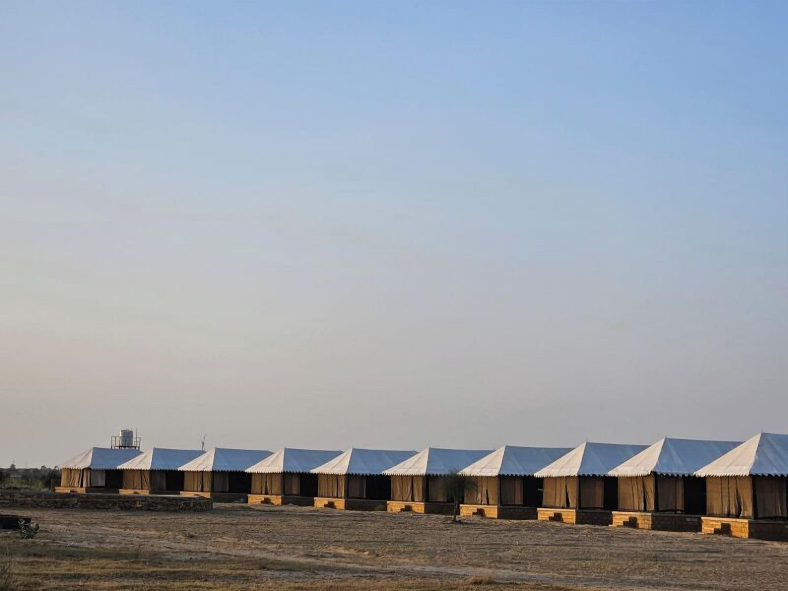 A row of yurts with a metal roof and wooden walls, arranged in a line on a dry, open field.