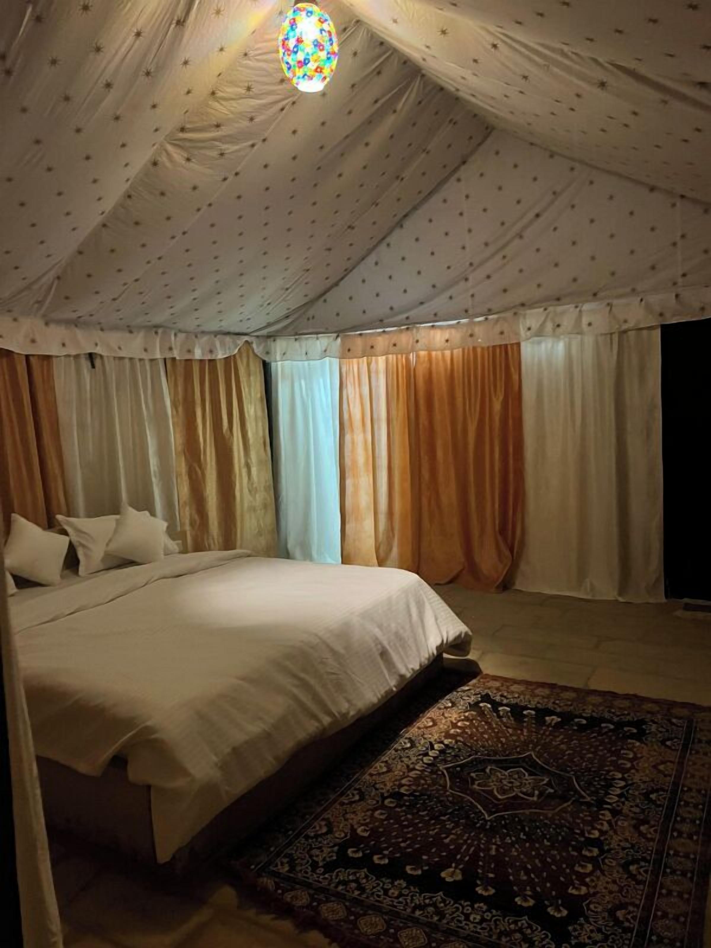 A bedroom with a bed, curtains, and a patterned rug.