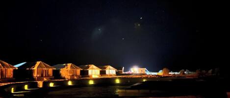 Varias yurtas iluminadas a lo largo de una masa de agua, de noche.