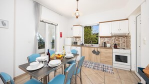 Une cuisine moderne avec des meubles blancs, un coin repas avec des chaises bleues et une vue sur la verdure à l’extérieur.