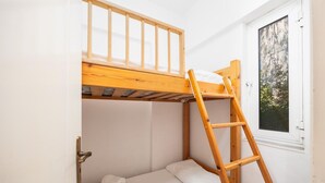 Un lit superposé avec une échelle en bois, une porte blanche et une fenêtre donnant sur des arbres.