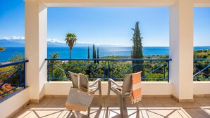 Un balcon avec vue sur la mer, deux chaises et une table.
