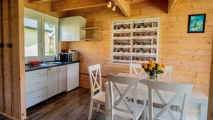 A wooden interior with a kitchen and dining area, featuring white cabinets, a wooden ceiling, and a window with a view. - Comfortable Holiday Homes With a Pool (Ustronie Morskie)