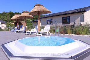 Een zwembad met ligbedden en parasols, een gebouw met een pannendak, en een omheind gebied met beplanting.