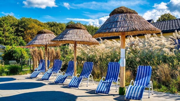 A poolside area with striped lounge chairs and thatched umbrellas. - Comfortable Holiday Homes With a Pool (Ustronie Morskie)