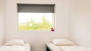 Ein kleines, sauberes Zimmer mit zwei Einzelbetten, einem Fenster mit Blick auf Grünflächen und einem schlichten, zweckmäßigen Design.