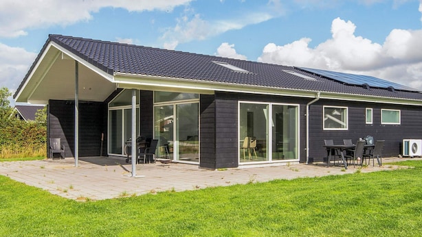 Ein modernes Haus mit einer überdachten Terrasse, großen Fenstern und Solaranlagen.