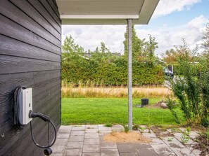 A wooden exterior wall with a power outlet and cable, a paved pathway leading to a grassy area, and a metal pole in the background. - 4 Star Holiday Home in Hemmet (Hemmet)