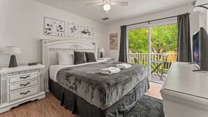 A bedroom with a bed, bedside tables, a ceiling fan, and a balcony with a view of greenery. - Magic Getaway at Emerald Island (Kissimmee)