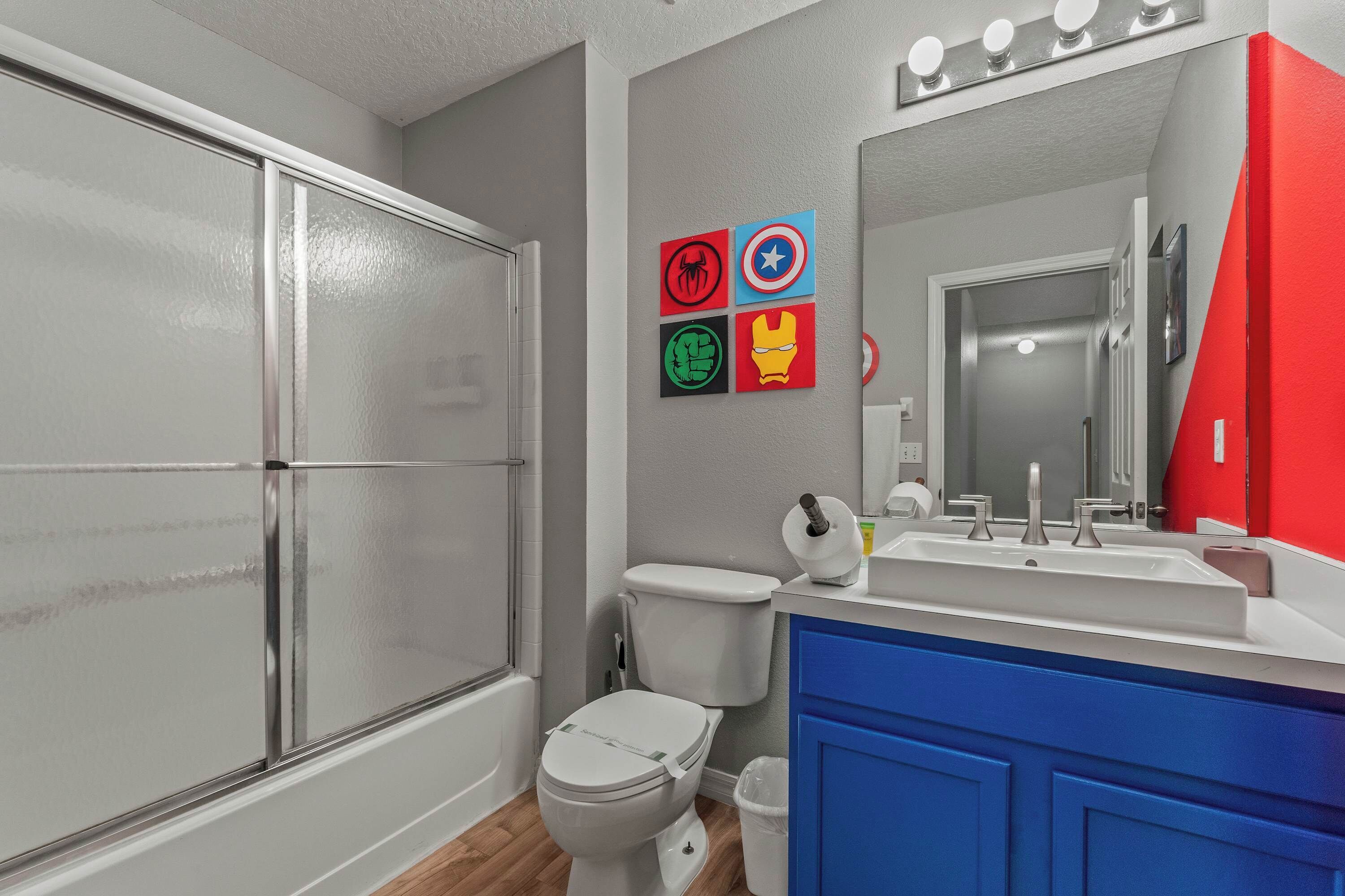 A bathroom with a glass shower enclosure, a toilet, a sink with a mirror, and a red cabinet.