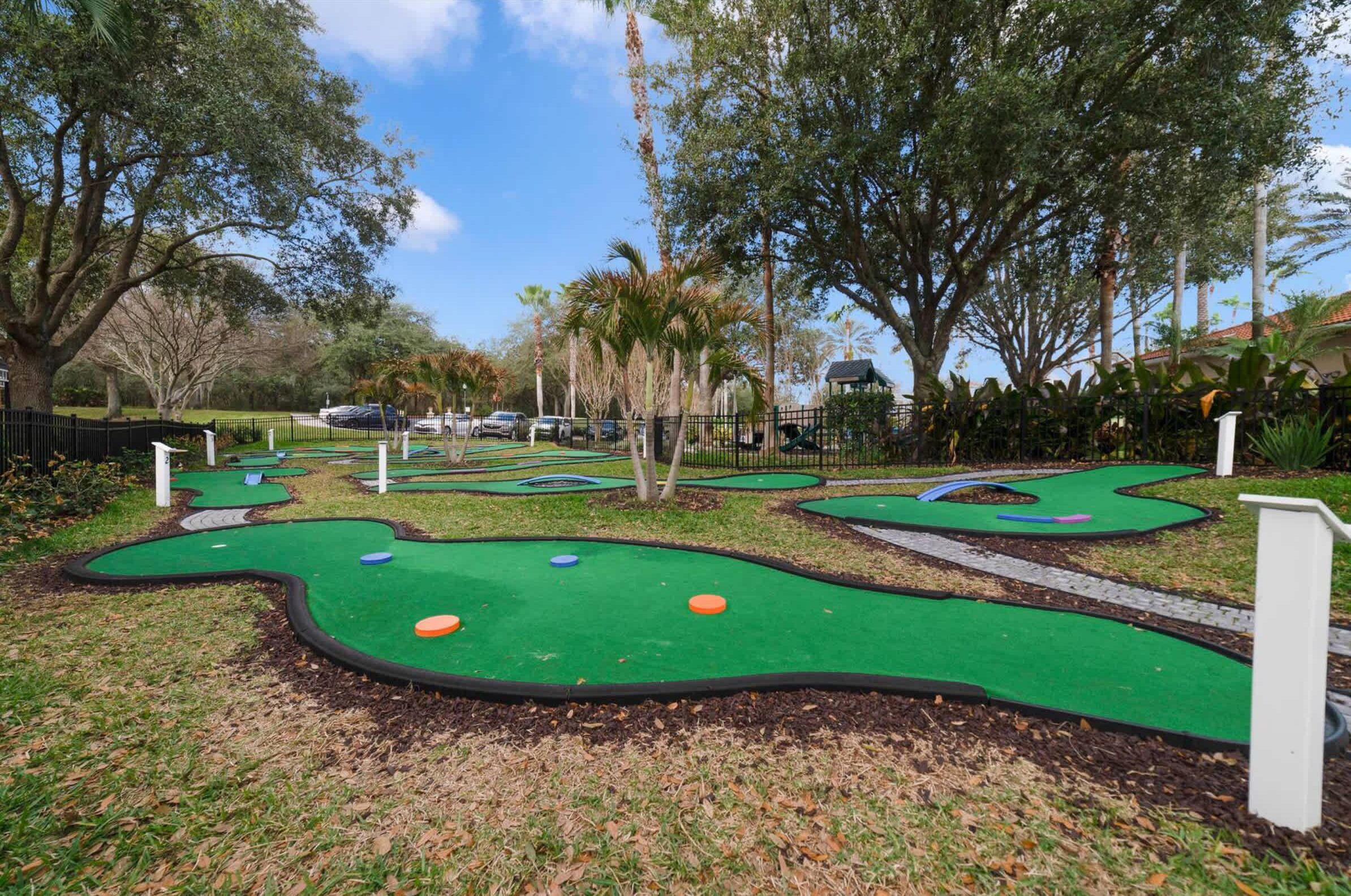 A miniature golf course with multiple holes, surrounded by trees and a clear sky.