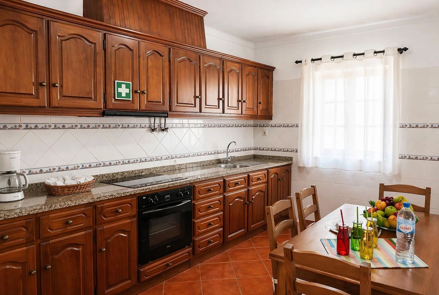 Una cocina con armarios de madera, horno empotrado, cafetera y comedor con una mesa dispuesta para dos.