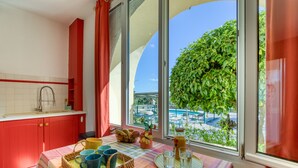 Eine Küche mit roten Schränken, einem Fenster mit Blick auf Pool und Grünanlage, und Frühstücksleckereien auf dem Tisch.