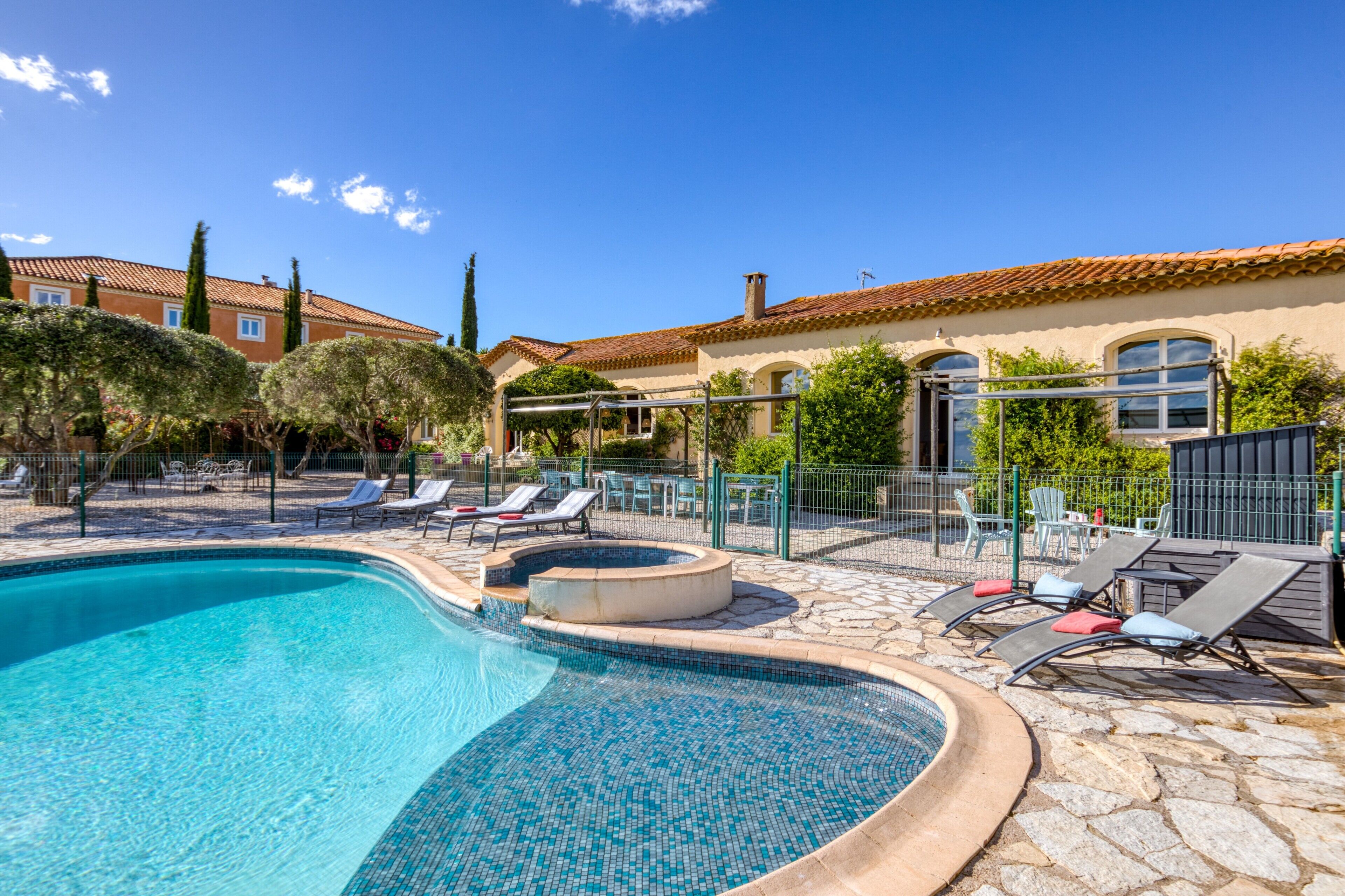 A swimming pool with lounge chairs, a stone deck, and a building with a tiled roof.