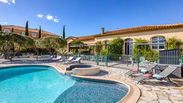A swimming pool with lounge chairs, a stone deck, and a building with a tiled roof.