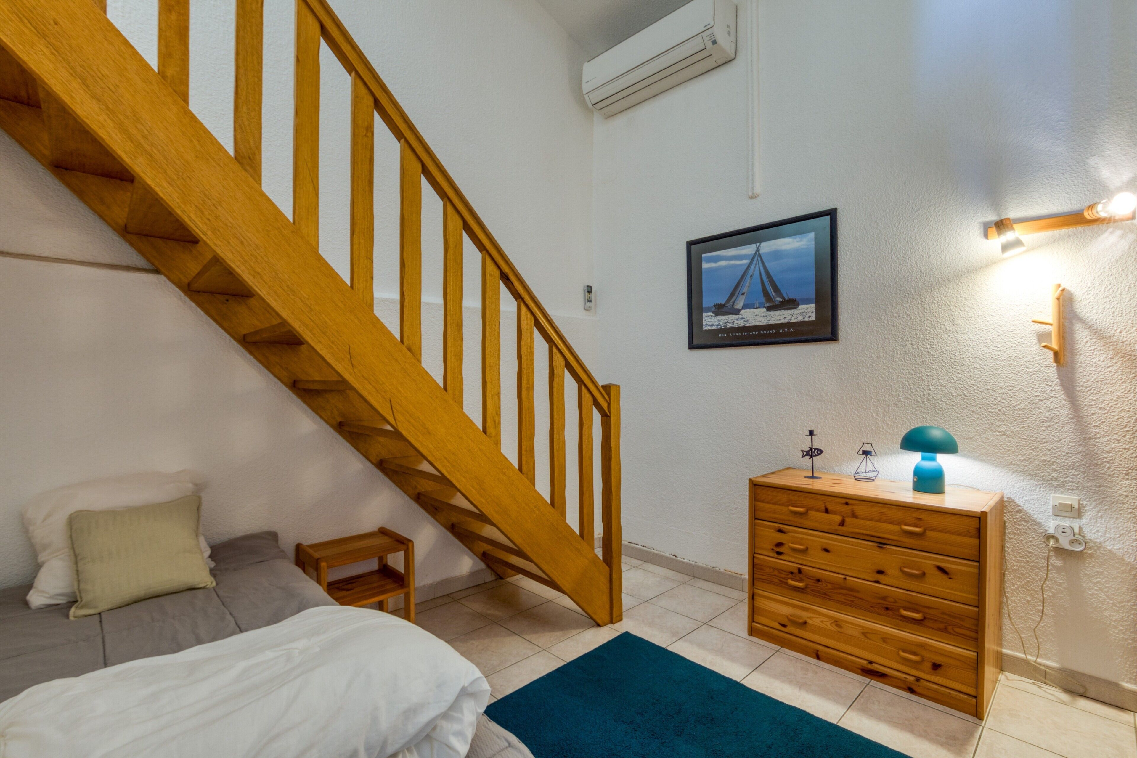 Una camera da letto con una scala in legno, un letto, una cassettiera, un tavolino e un quadro appeso al muro.