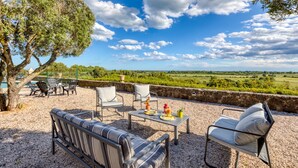 Ein Außenbereich mit Tisch und Stühlen, einer Couch und Blick auf die Landschaft.