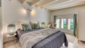 Ein Schlafzimmer mit Bett, Nachttischen, einem Fenster mit Vorhängen und Blick ins Grüne.