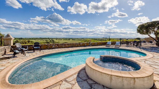 Ein Pool mit geschwungener Form, umgeben von Steinplatten und Gartenmöbeln.