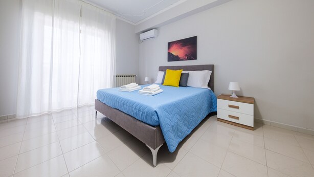 A bedroom with a bed, a nightstand, a radiator, and a window with curtains.